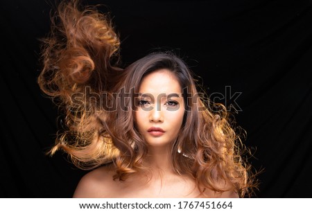Portrait Head shot of 20s tanned skin young asian woman blonde hair and blow fluttering hair in air with blower, look at camera over black drape curtain background