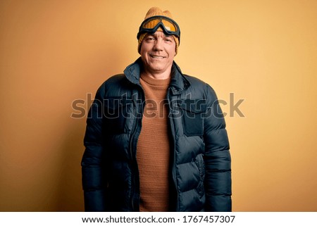 Middle age handsome grey-haired skier man on vacation wearing ski goggles with a happy and cool smile on face. Lucky person.