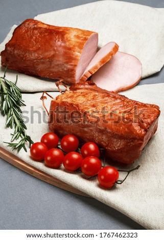 Natural smoked ham lying on a rustic linen cloth, complete with fresh rosemary and a branch of cherry tomatoes.  Natural product from an organic farm, produced using traditional methods.
