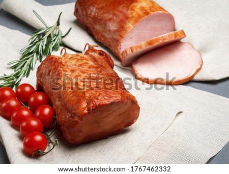 Natural smoked ham lying on a rustic linen cloth, complete with fresh rosemary and a branch of cherry tomatoes.  Natural product from an organic farm, produced using traditional methods.