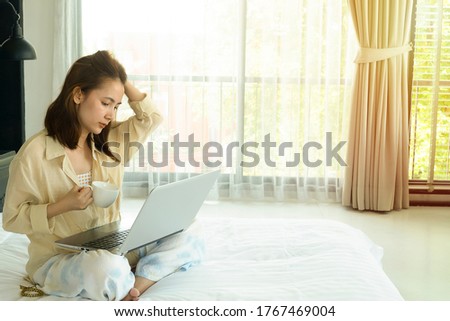 A girl using laptop on the bed and drink coffee in the morning, work at home, shopping online, woman have a problem and unhappy feeling