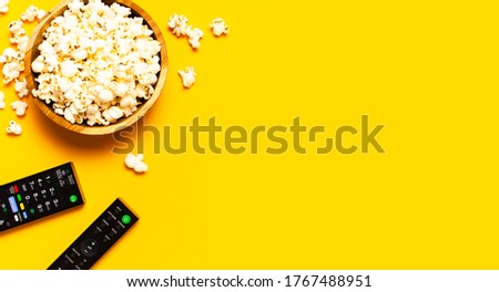 
Black TV, audio remote control and popcorn on bright yellow background flat lay top view copy space. Minimalistic background with a remote control, watching a movie, series set-top boxes audio system