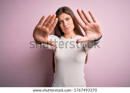 Young beautiful woman with blue eyes wearing casual white t-shirt over pink background doing frame using hands palms and fingers, camera perspective