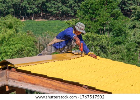 Close-up photos of a mechanic who is roofing and using screws, electric drills and roof installation