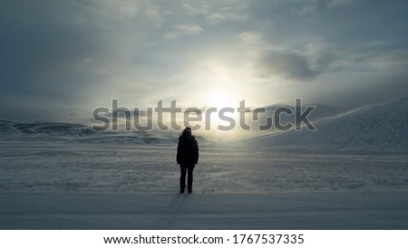 Concept picture of silhouette alone woman standing on white road facing the sunlight that hidden in the clouds above snow mountain