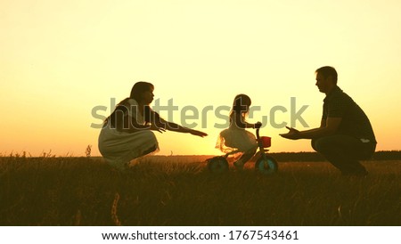 Mom and dad teach a young child to ride a bike at sunset in the park. Teamwork. Silhouette family walk.