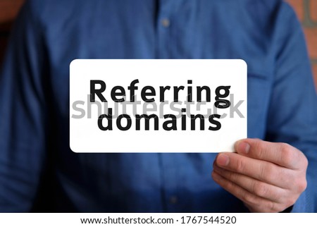Referring domains - seo concept text on a white sign in the hand of a man in a blue shirt