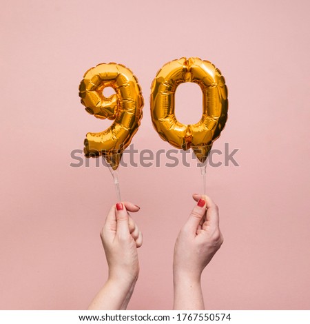 Female hand holding a number 90 birthday anniversary celebration gold balloon