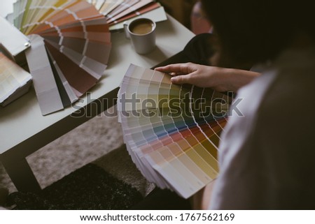 Woman choosing paint color from swatches and palette for house renovation and repair, drinking coffee.