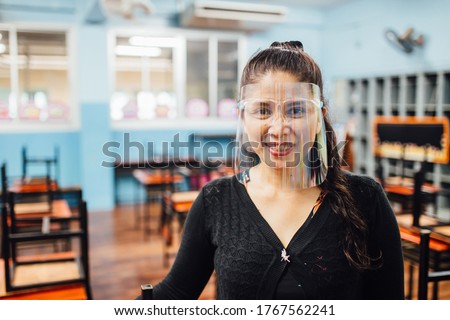 Portrait of beautiful Asian female teacher wearing face shield smiling while standing  in classroom. New normal lifestyle during corona virus or Covid-19 crisis Royalty-Free Stock Photo #1767562241
