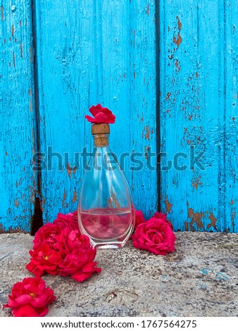 
Transparent glass water bottle stands on gray concrete with red roses lying nearby on a blue wooden background from boards