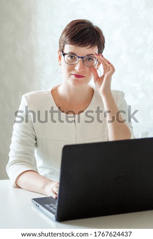 A young woman with a short haircut and glasses works on a laptop from her home. Remote workplace, freelance. Distance learning