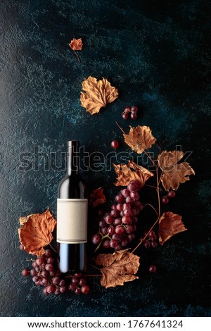 Bottle of red wine with ripe grapes and dried up vine leaves. Old dark blue background. On a bottle old empty label. Copy space, top view.
