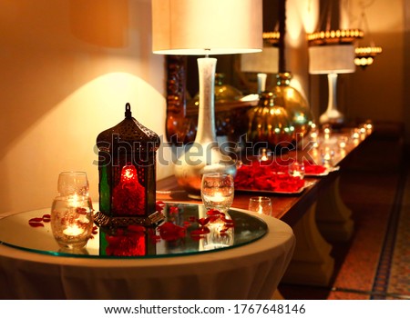 Beautiful arabic hotel reception decoration with oriental candle for Ramadan, wedding, corporate party with rose flower petals, warm lamp light and glasses, evening interior decor   Royalty-Free Stock Photo #1767648146