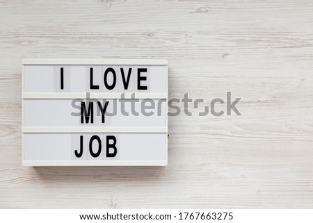 'I love my job' on a lightbox on a white wooden surface, top view. Flat lay, from above, overhead. Copy space.