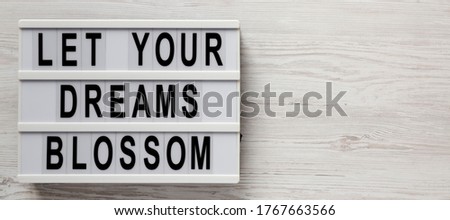 'Let your dreams blossom' on a lightbox on a white wooden background, top view. Space for text.