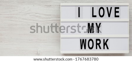 'I love my work' on a lightbox on a white wooden background, top view. Flat lay, from above, overhead. Copy space.