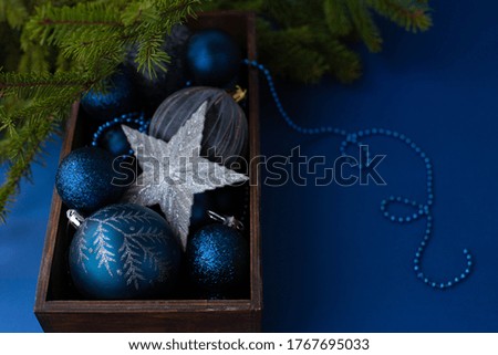 Classic blue Christmas toy balls with sparkles, snowflakes and big silver star in a wooden box on a background with beads and green fir new year tree branches.