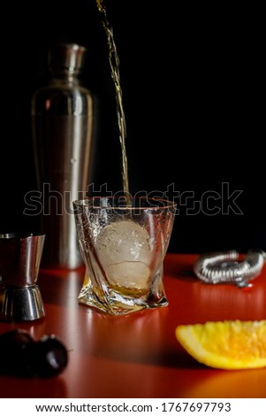 Picture of bourbon poured into a glass with a big ice cube and bar essentials