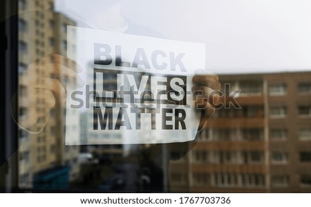Man holding "Black lives matter" sign behind the window during Covid-19 quarantine.
