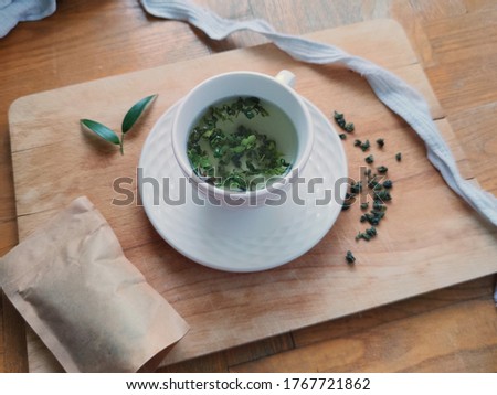 Classic loose leaf green tea with fresh leaves brewed in a white modern teapot viewed from above, lifestyle picture with tea leaves and packaging, hot brew green Chinese tea in a cup on wood
