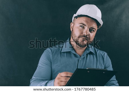 A man in a construction helmet signs a document on a dark background