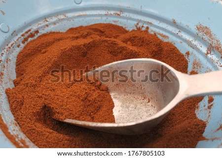 Dried and ground cocoa beans in a small metal bowl with a spoon. The dried cocoa beans are ground to a paste or powder, which is used to prepare meals and desserts.
