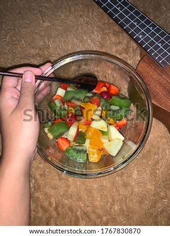 Colourfull fruit are served in the glass bowl and put it on the brown carpet behind the ukulele there