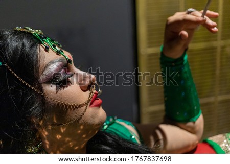 Drag queen posing in apartment in green Indian sari dress. A wig with Black long hair, accessories and make up. High quality photo