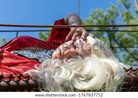 Drag queen posing on a iron construction in red dress. A wig with white long hair and make up. High quality photo