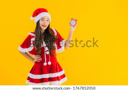 Portrait beautiful young asian woman wear christmas clothes and hat show clock or alarm on yellow isolated background