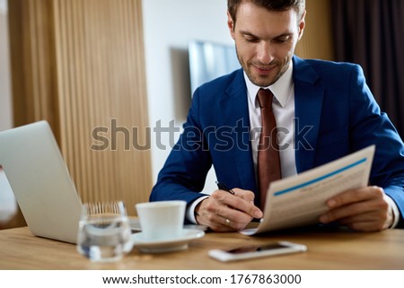 Happy businessman going through paperwork and signing documents in a hotel room. 