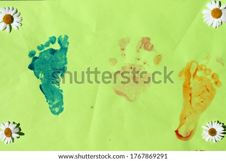 Imprints of the arms and legs of a child, red, yellow and blue, decorated with white flowers, against a green background.
