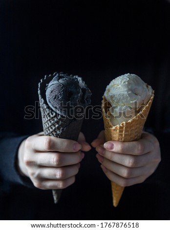 Black ice cream and white ice cream in a waffle cup in female hands. Fashionable food. Copy space