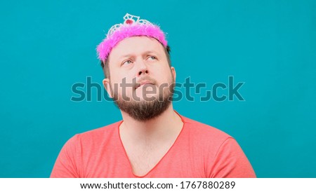 Playful bearded freaky man in a pink T-shirt with a deadema on his head sad with a magic wand in his hand. A funny wizard joke to make and fulfill a wish