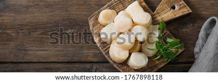 Scallops on a wooden Board on a brown wooden table close-up. Top view with space for text. Banner Royalty-Free Stock Photo #1767898118