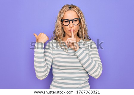 Beautiful blonde woman wearing casual striped t-shirt and glasses over purple background asking to be quiet with finger on lips pointing with hand to the side. Silence and secret concept.