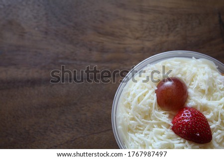 Fresh fruit salad of melon, grape, strawberry, kiwi dressed with yoghurt  chopped Apple. cheese and fruits for upper topping. served in a square plastic on wooden tray. selective focus