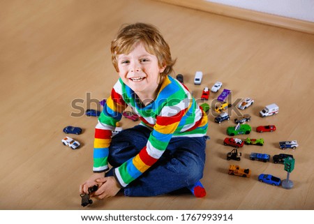 Lovely blond kid boy playing with lots of toy cars indoor. Happy healthy child boy having fun during pandemic coronavirus quarantine disease. Child alone at home, closed nursery.