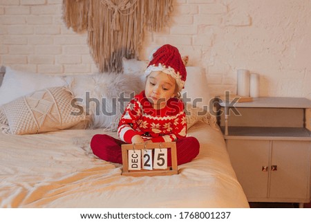 Little girl in a New Year's hat and a sweater sits on a bed.
Merry christmas and happy new year