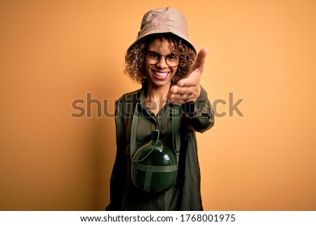 Young african american tourist woman on vacation wearing explorer hat and water canteen smiling friendly offering handshake as greeting and welcoming. Successful business. Royalty-Free Stock Photo #1768001975