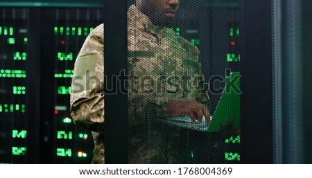 Close up of young African American military officer checking work of servers in analytic monioring center. Man with laptop computer control networking in dark room Cybersecurity in army concept. Royalty-Free Stock Photo #1768004369