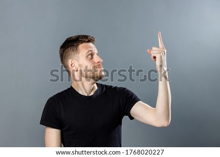 Young man with a surprised face is showing something interesting on grey background.