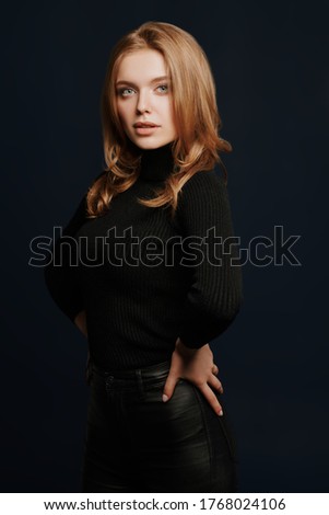 Beauty portrait. Gorgeous young woman with blonde hair and beautiful blue eyes posing in black turtleneck on a dark blue background. 