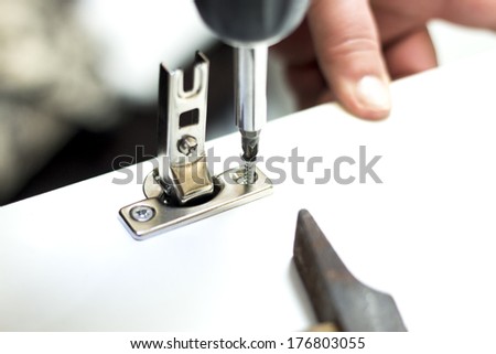 A carpenter builds a small white cabinet with a screwdriver  Royalty-Free Stock Photo #176803055