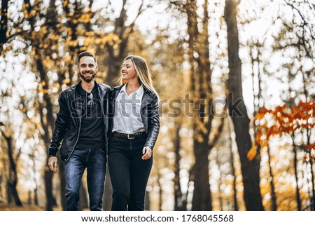 Beautiful young couple walking in the autumn park on a sunny day. They hug and smile, enjoy a walk.