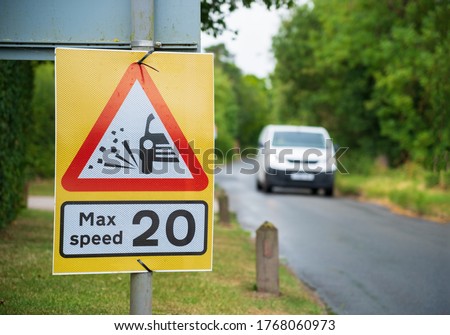 "Max speed 20" Temporary road sign on a village road with a vehicle
approaching in an out of focus background.