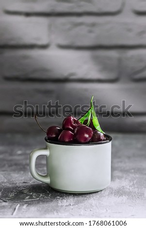 Ripe cherry berries in a white mug on a background of a brick wall. Harvest summer berries. Copy space.