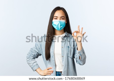 Social distancing lifestyle, covid-19 pandemic everyday life concept. Satisfied confident asian girl have all under control, guarantee and encourage everything good with okay sign, wear mask
