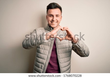 Young handsome caucasian man wearing casual winter jacket standing over isolated background smiling in love showing heart symbol and shape with hands. Romantic concept.